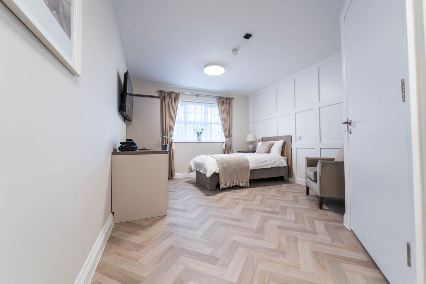 A bright bedroom with herringbone floor, bed and armchair