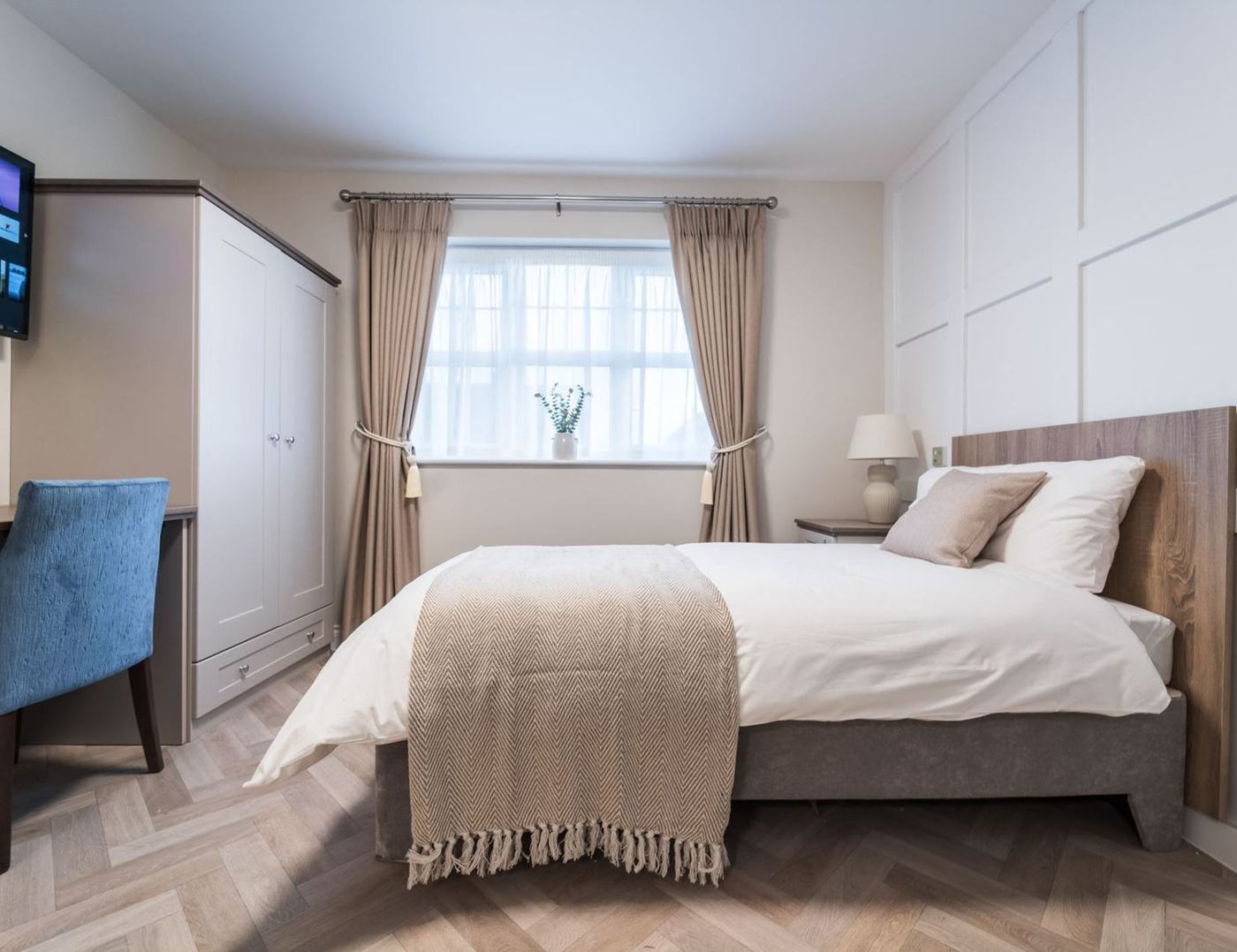 A bright double bedroom with a wardrobe, desk, soft furnishings and herringbone floor