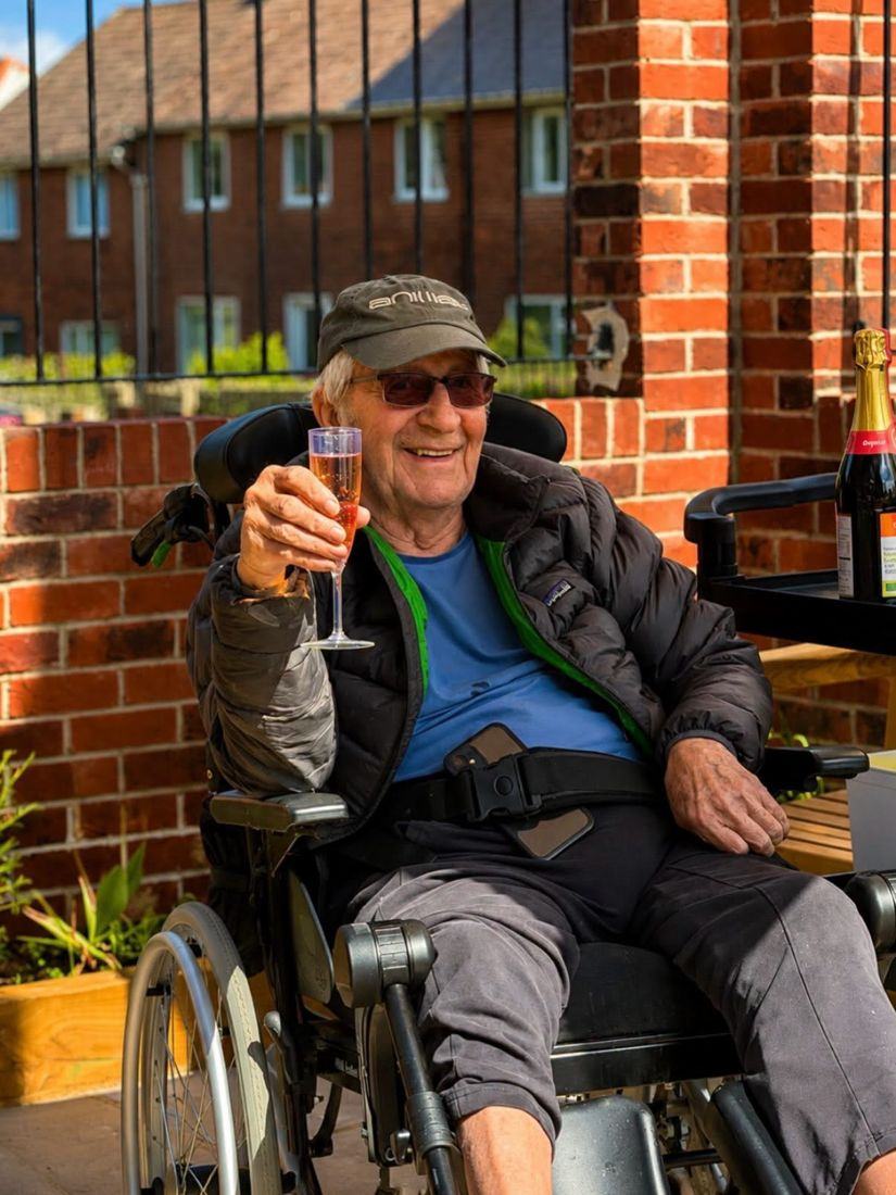 A smiling resident raising a glass of fizz in the courtyard garden
