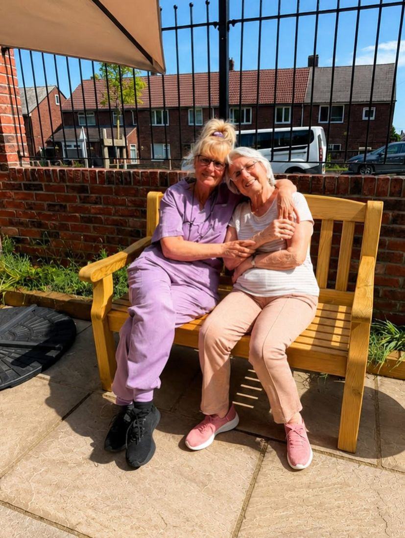 A carer and a resident sharing a hug on a garden bench in the sunshine