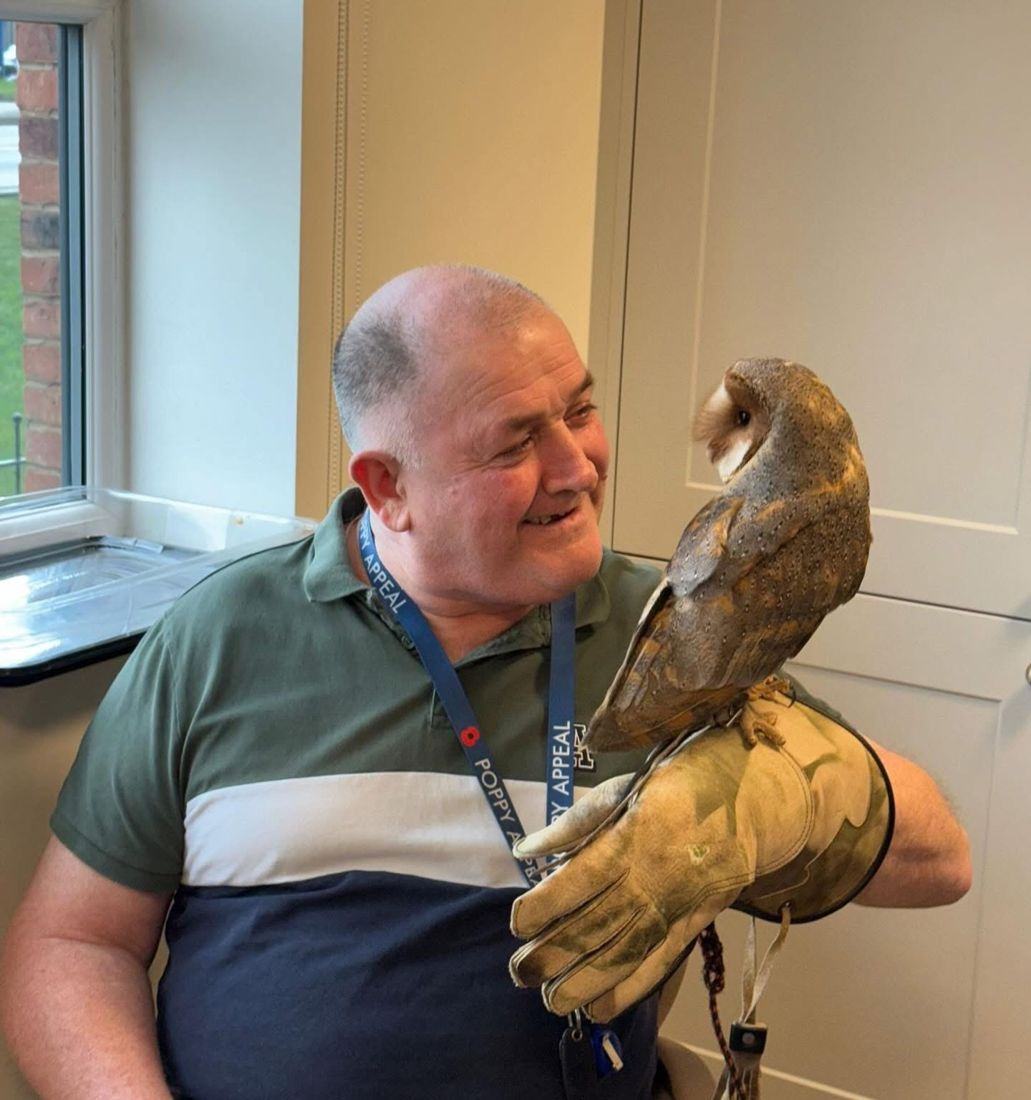 A smiling visitor holding a barn owl on a falconry glove