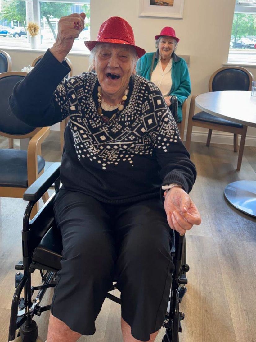A smiling resident in a red party hat dancing in her chair