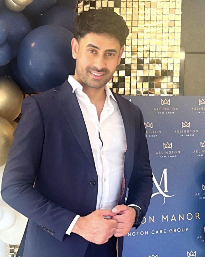 Vinny Sandhu, Managing Director, smiling in a navy suit in front of an Arlington Care Group backdrop